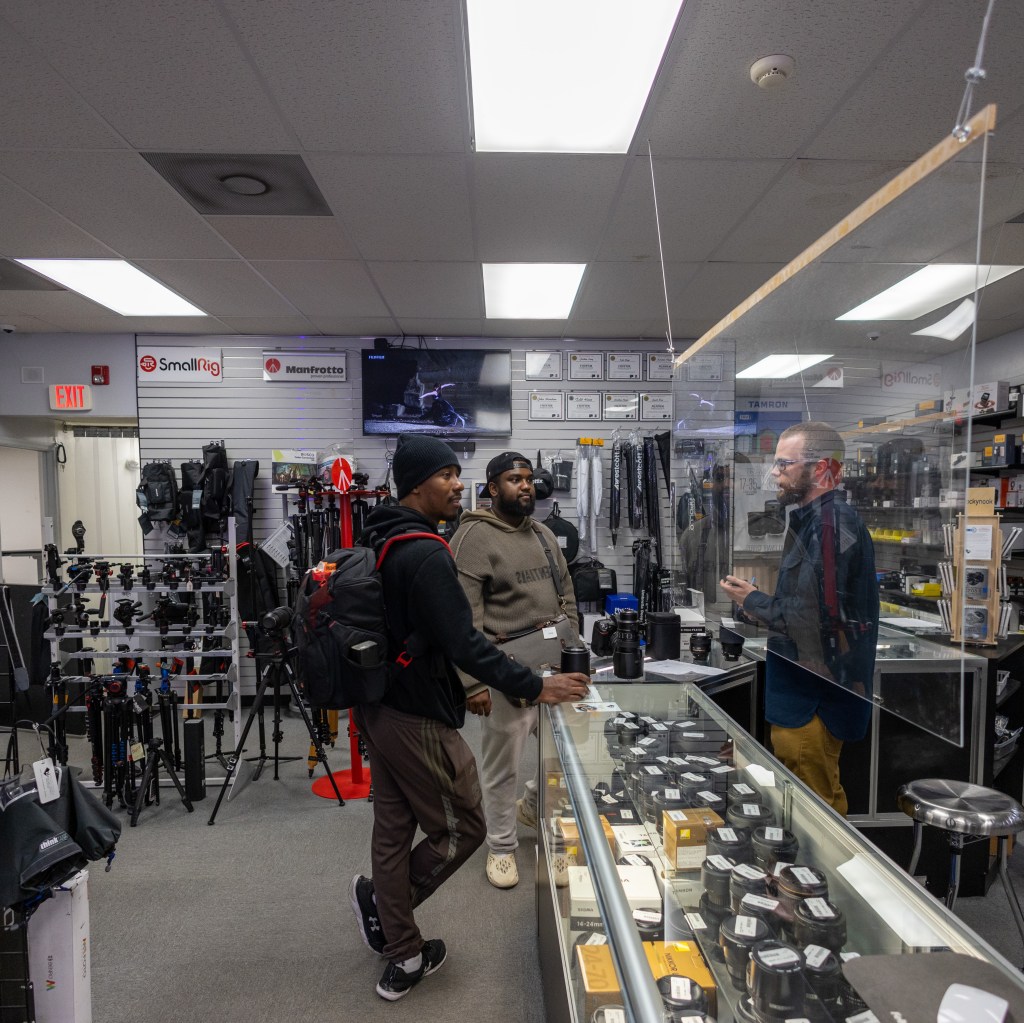 Three people talking beside camera and lens displays in a photography shop