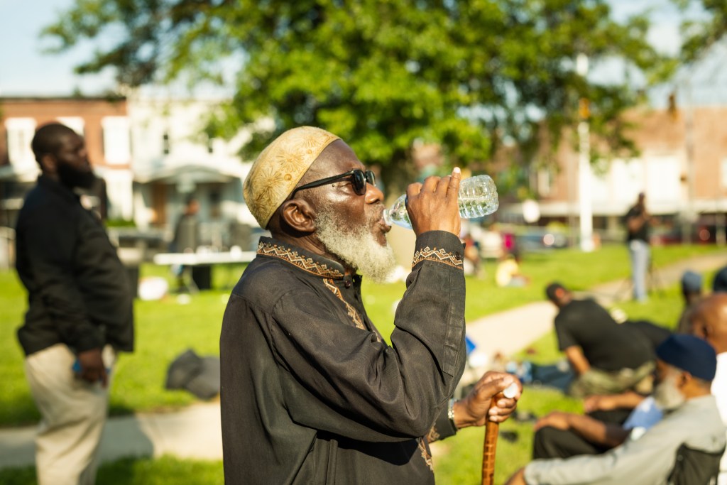 A man with a walking stick drinking water at an outdoor gathering