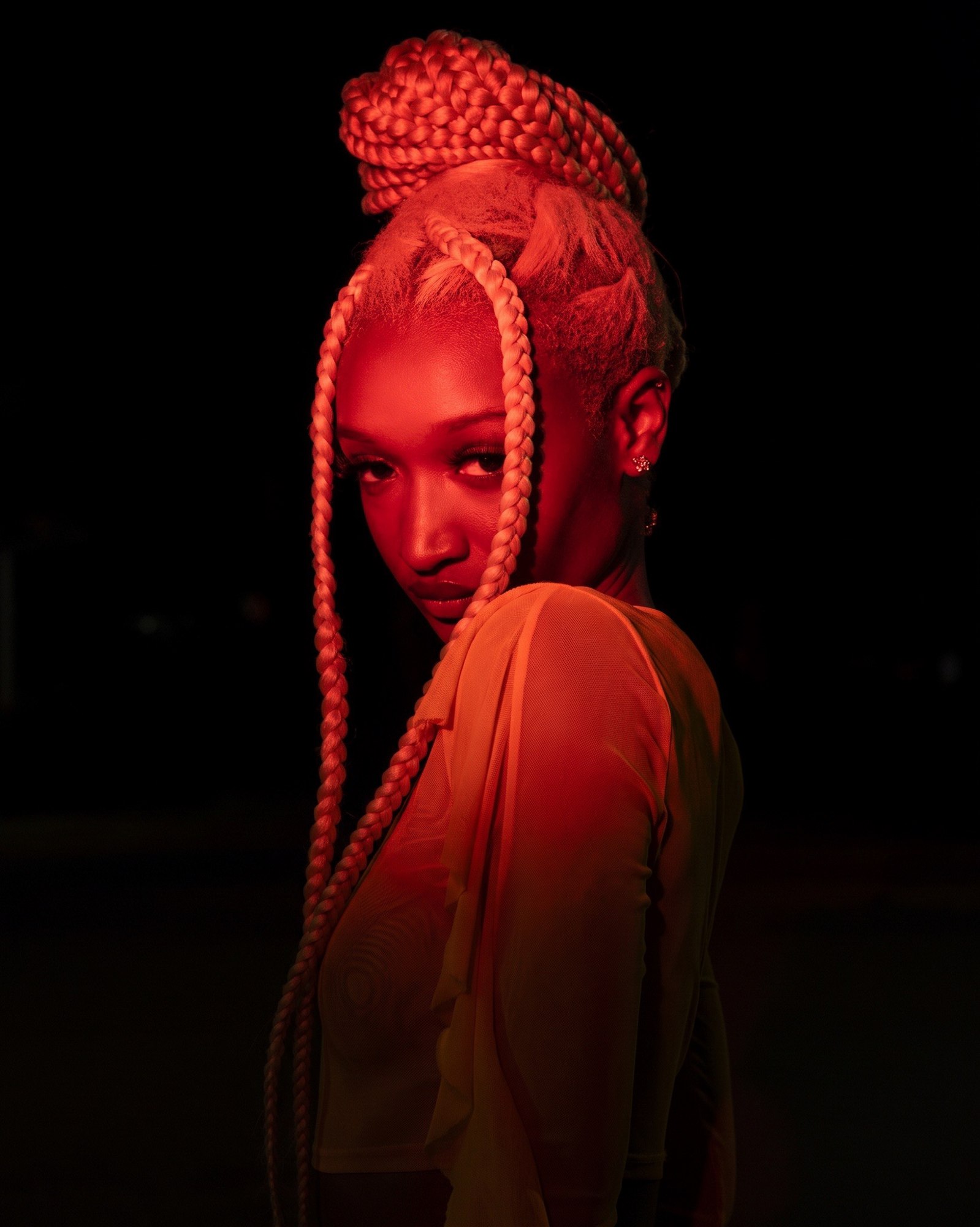 Signature red-lit studio portrait with braids, photographed by Adib Abdussalaam